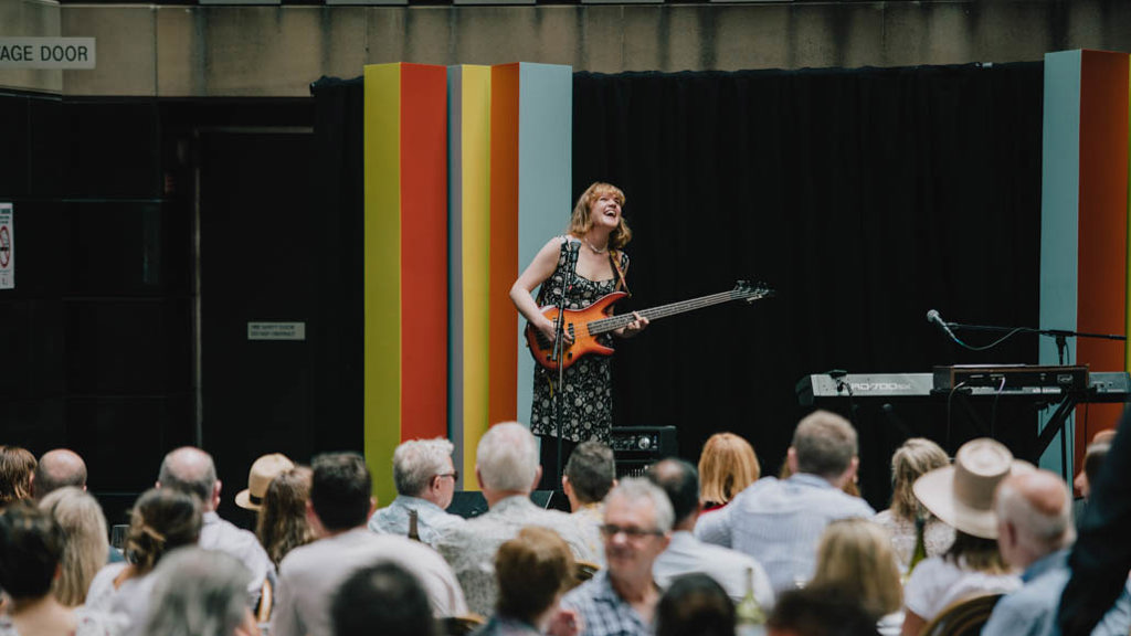 Sweet Whirl performing on bass guitar at City Recital Hall's outdoor stage
